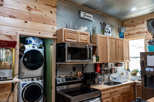 kitchen featuring stainless steel appliances, light countertops, a sink, wood walls, and stacked washing maching and dryer