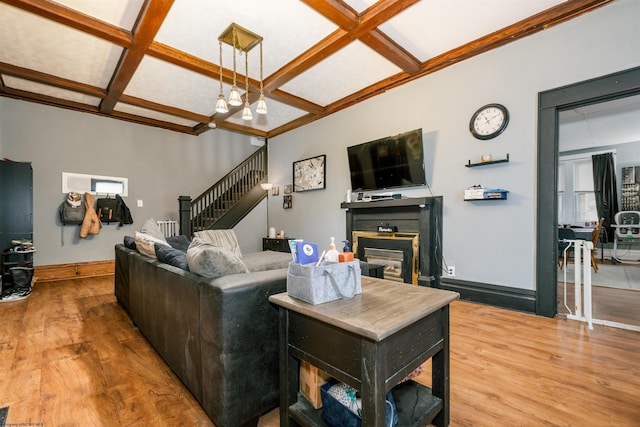 living area with stairs, coffered ceiling, wood finished floors, and a glass covered fireplace