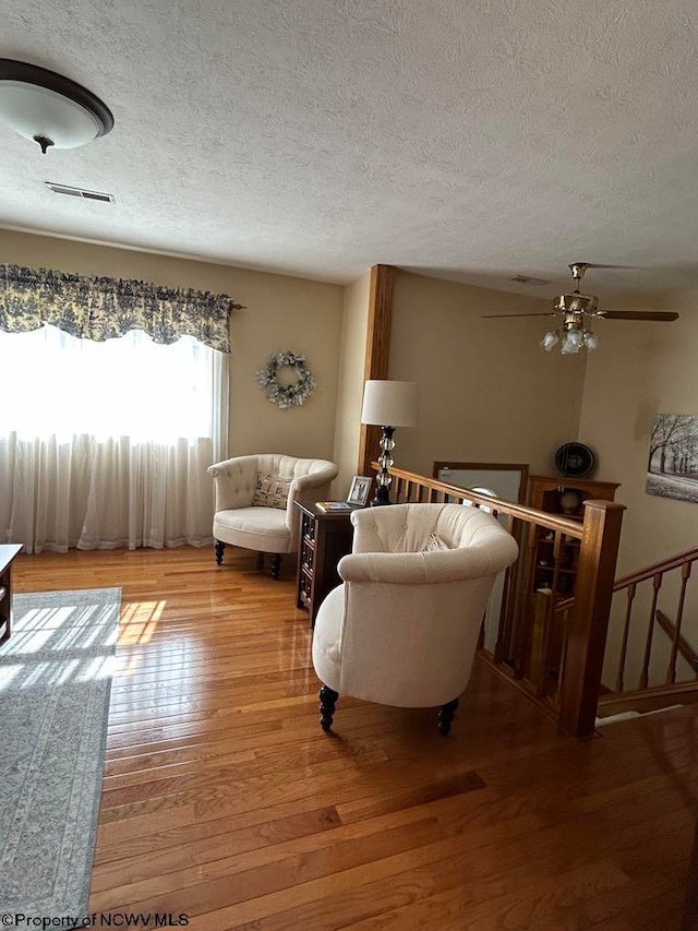 living room with a ceiling fan, visible vents, a textured ceiling, and hardwood / wood-style floors