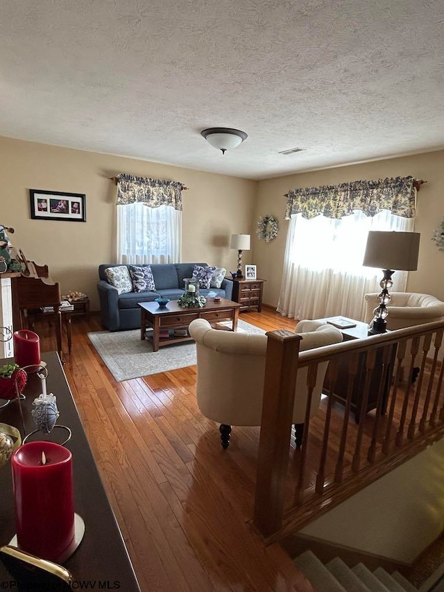 living area with a wealth of natural light, light wood-type flooring, visible vents, and a textured ceiling