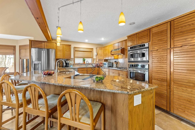 kitchen with stainless steel appliances, brown cabinetry, a sink, and tasteful backsplash