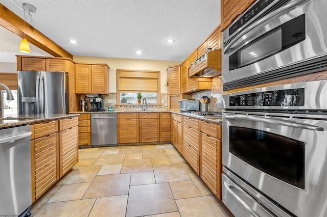 kitchen featuring a textured ceiling, light stone counters, a sink, appliances with stainless steel finishes, and decorative backsplash