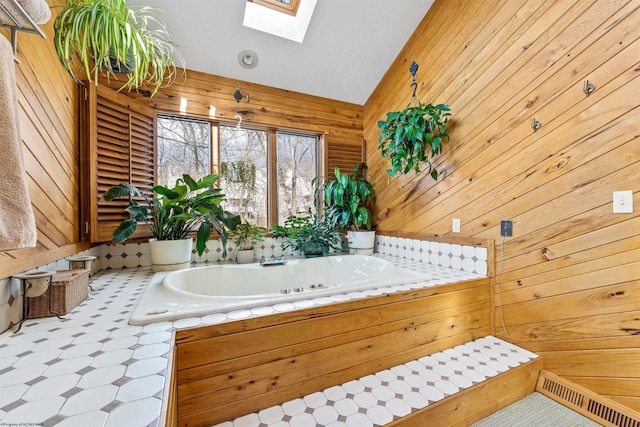 full bath featuring vaulted ceiling with skylight, a tub with jets, visible vents, and wooden walls