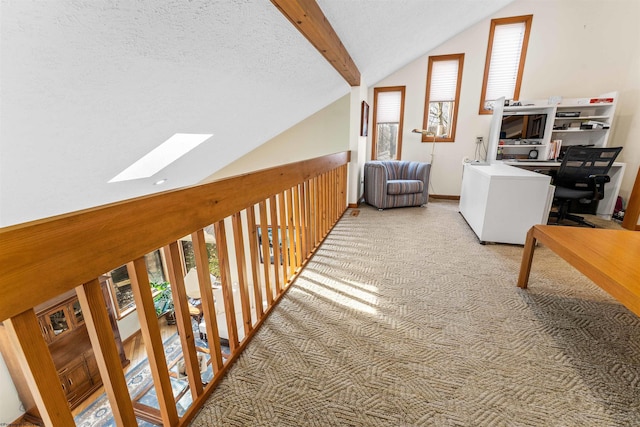 corridor featuring carpet, vaulted ceiling with skylight, baseboards, and a textured ceiling