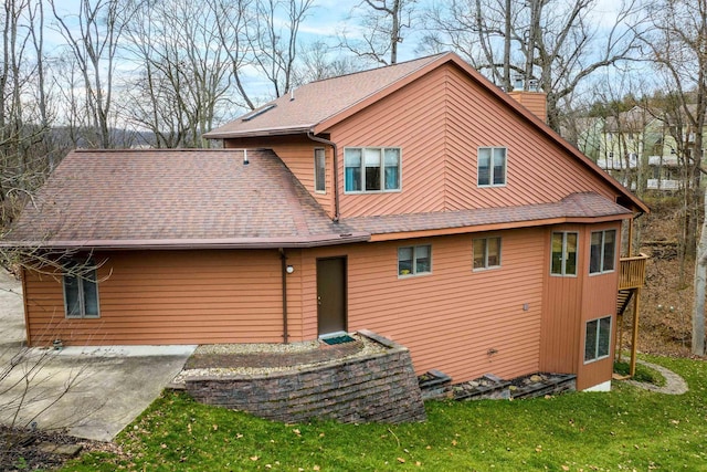 back of house with a yard, a chimney, and roof with shingles