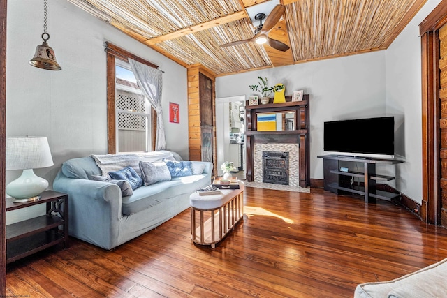 living area with a stone fireplace, wooden ceiling, a ceiling fan, baseboards, and wood-type flooring