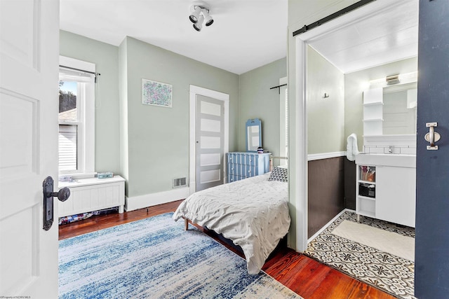 bedroom featuring a barn door, radiator heating unit, wood finished floors, and baseboards