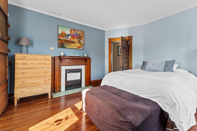 bedroom featuring a fireplace with flush hearth, visible vents, ornamental molding, and hardwood / wood-style floors