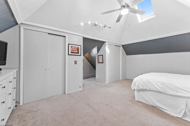 carpeted bedroom with lofted ceiling with skylight, a ceiling fan, and wooden walls