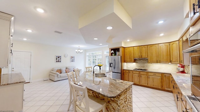 kitchen featuring stainless steel fridge, tasteful backsplash, light stone countertops, gas cooktop, and a sink