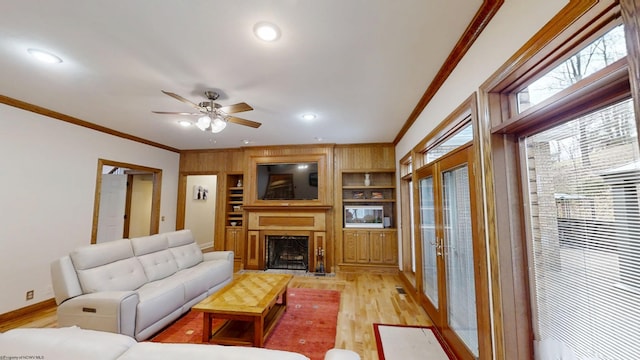 living room featuring built in shelves, a fireplace, light wood finished floors, ornamental molding, and baseboards