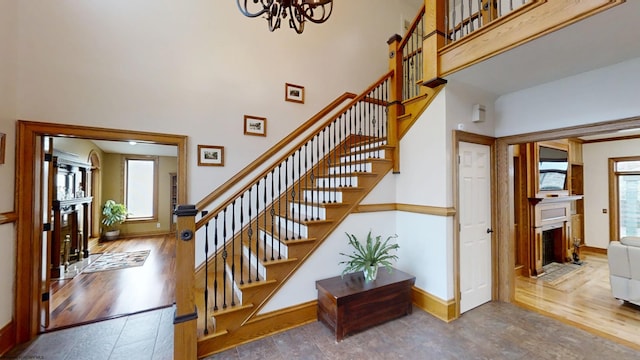 staircase with a fireplace with flush hearth, a high ceiling, baseboards, and wood finished floors