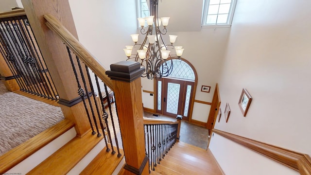 stairs with baseboards, wood finished floors, and an inviting chandelier