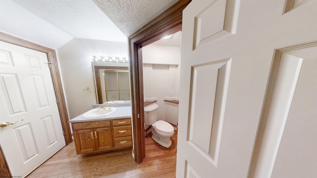 bathroom with toilet, vaulted ceiling, vanity, a textured ceiling, and wood finished floors