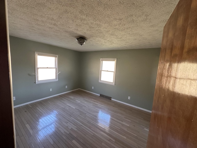 unfurnished room featuring dark wood-type flooring, a wealth of natural light, visible vents, and baseboards