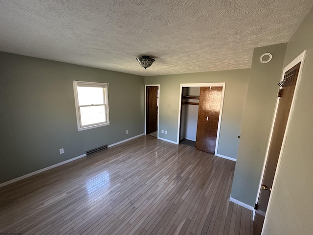 unfurnished bedroom with dark wood-style floors, multiple closets, visible vents, a textured ceiling, and baseboards