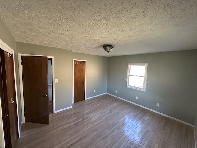 unfurnished bedroom featuring dark wood-style floors, baseboards, a textured ceiling, and two closets