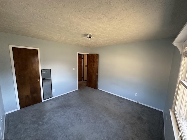 unfurnished bedroom with a textured ceiling, dark colored carpet, and baseboards