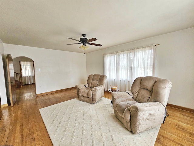 sitting room with light wood-type flooring, baseboards, arched walkways, and a ceiling fan