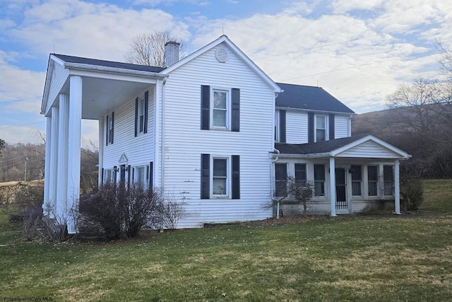 view of front of house with a front lawn, a chimney, and a sunroom