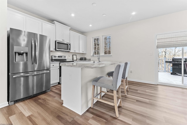 kitchen with appliances with stainless steel finishes, a breakfast bar, light wood-type flooring, and white cabinetry