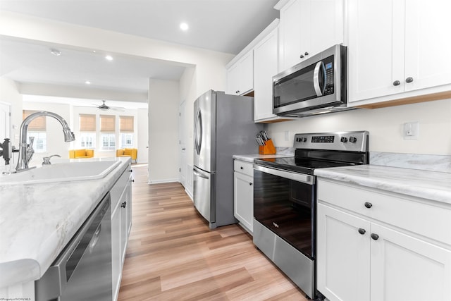 kitchen featuring a ceiling fan, stainless steel appliances, light wood-type flooring, white cabinetry, and a sink