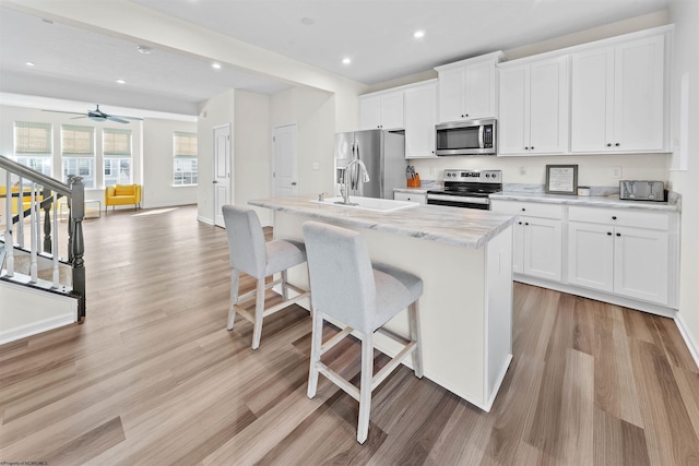 kitchen with stainless steel appliances, a kitchen bar, a center island with sink, and white cabinetry