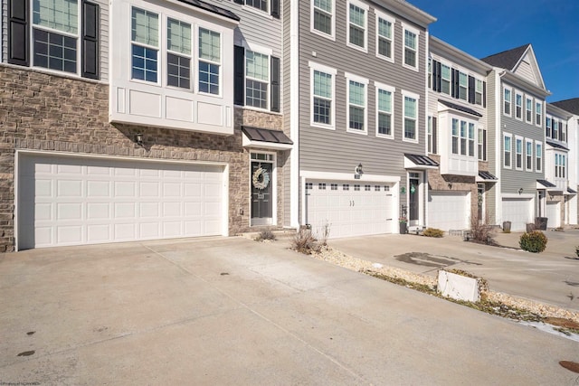 view of property featuring a garage, stone siding, a residential view, and driveway