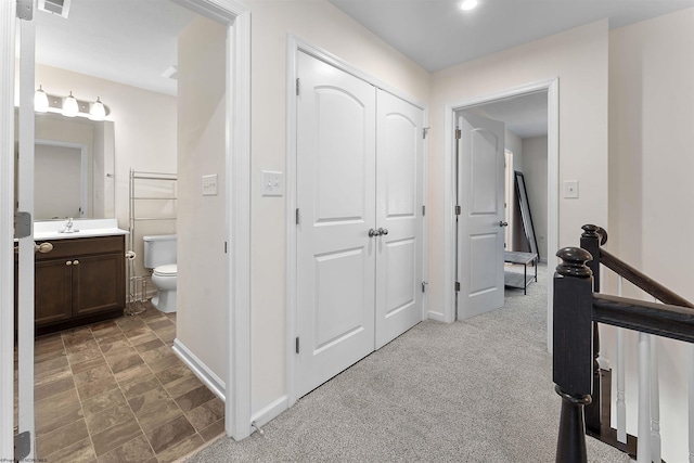 hall featuring carpet, baseboards, a sink, and an upstairs landing