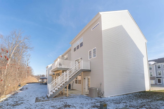 snow covered rear of property with stairs, central AC unit, and a deck