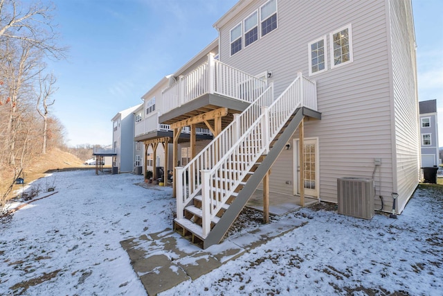 snow covered house with cooling unit, stairway, and a wooden deck