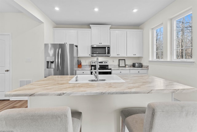 kitchen with a breakfast bar, a center island with sink, appliances with stainless steel finishes, and white cabinets