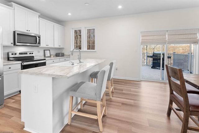 kitchen with light wood finished floors, appliances with stainless steel finishes, a breakfast bar, a kitchen island with sink, and a sink