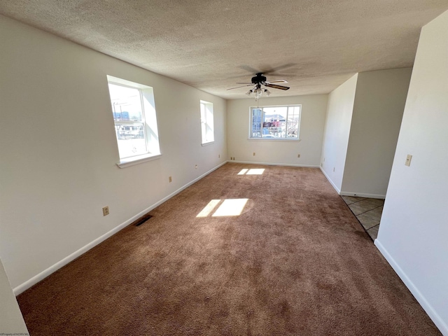 empty room with a textured ceiling, light colored carpet, a ceiling fan, baseboards, and visible vents