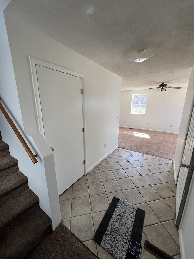 entryway featuring stairway, light carpet, light tile patterned flooring, ceiling fan, and a textured ceiling