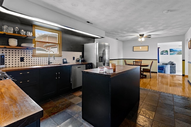 kitchen featuring dark cabinets, stainless steel appliances, stone tile flooring, wooden counters, and a sink