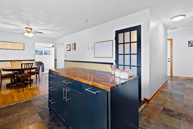 kitchen with stone tile floors, baseboards, a ceiling fan, butcher block counters, and blue cabinets