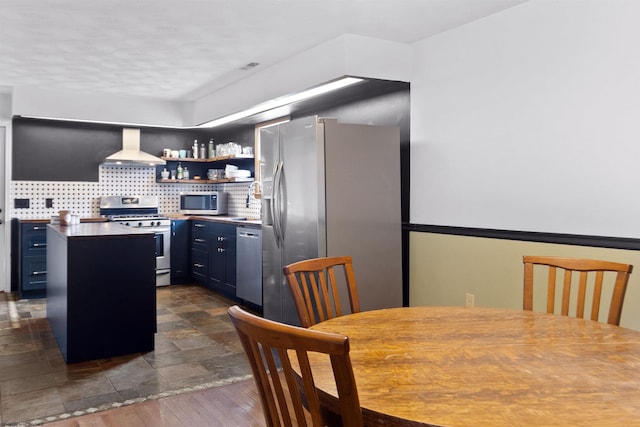 kitchen featuring blue cabinets, stainless steel appliances, backsplash, a center island, and wall chimney exhaust hood