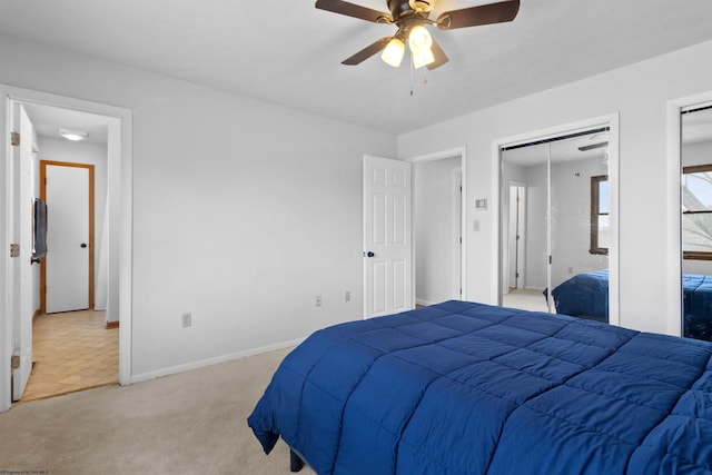 bedroom with baseboards, ceiling fan, multiple closets, and light colored carpet