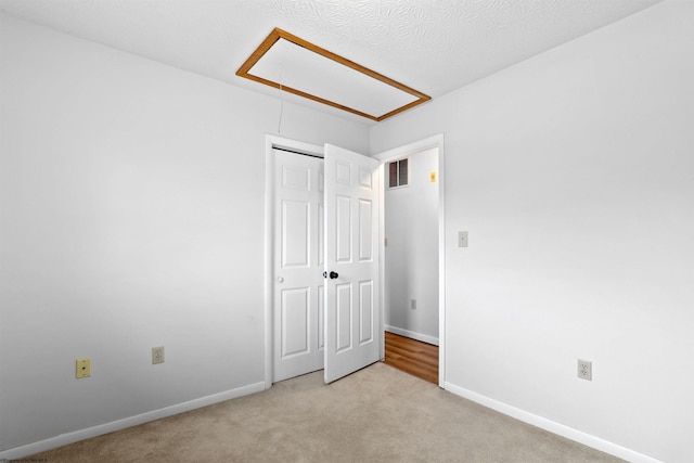 unfurnished bedroom with attic access, visible vents, baseboards, light colored carpet, and a closet