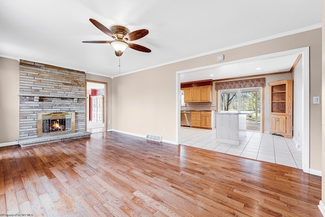 unfurnished living room with light wood-style floors, baseboards, ornamental molding, and a stone fireplace