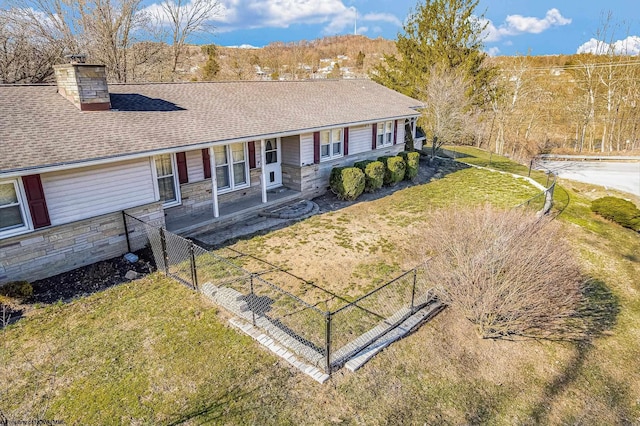 ranch-style home featuring stone siding, roof with shingles, a chimney, and a front lawn