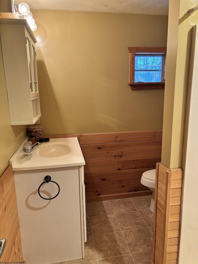 half bathroom featuring toilet, wooden walls, vanity, and wainscoting