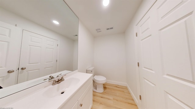 half bath featuring visible vents, toilet, vanity, wood finished floors, and baseboards