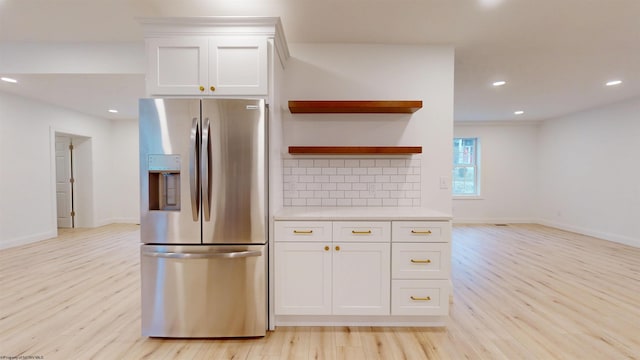 kitchen with stainless steel fridge, white cabinets, light countertops, light wood-style floors, and backsplash