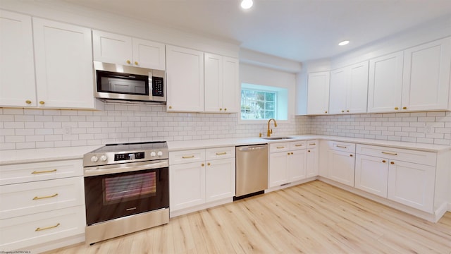 kitchen featuring light wood finished floors, appliances with stainless steel finishes, a sink, light countertops, and backsplash