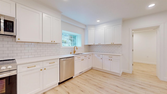 kitchen with light countertops, backsplash, appliances with stainless steel finishes, a sink, and light wood-type flooring