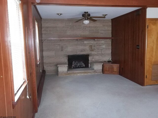 unfurnished living room featuring wooden walls, a healthy amount of sunlight, carpet floors, a fireplace, and a ceiling fan