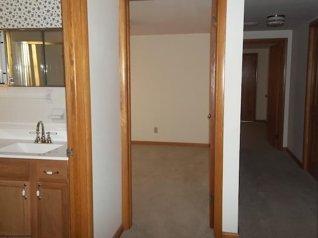 hallway featuring a sink, baseboards, and carpet flooring