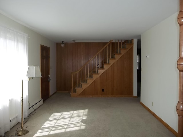 spare room featuring baseboards, stairs, wood walls, light carpet, and a baseboard heating unit